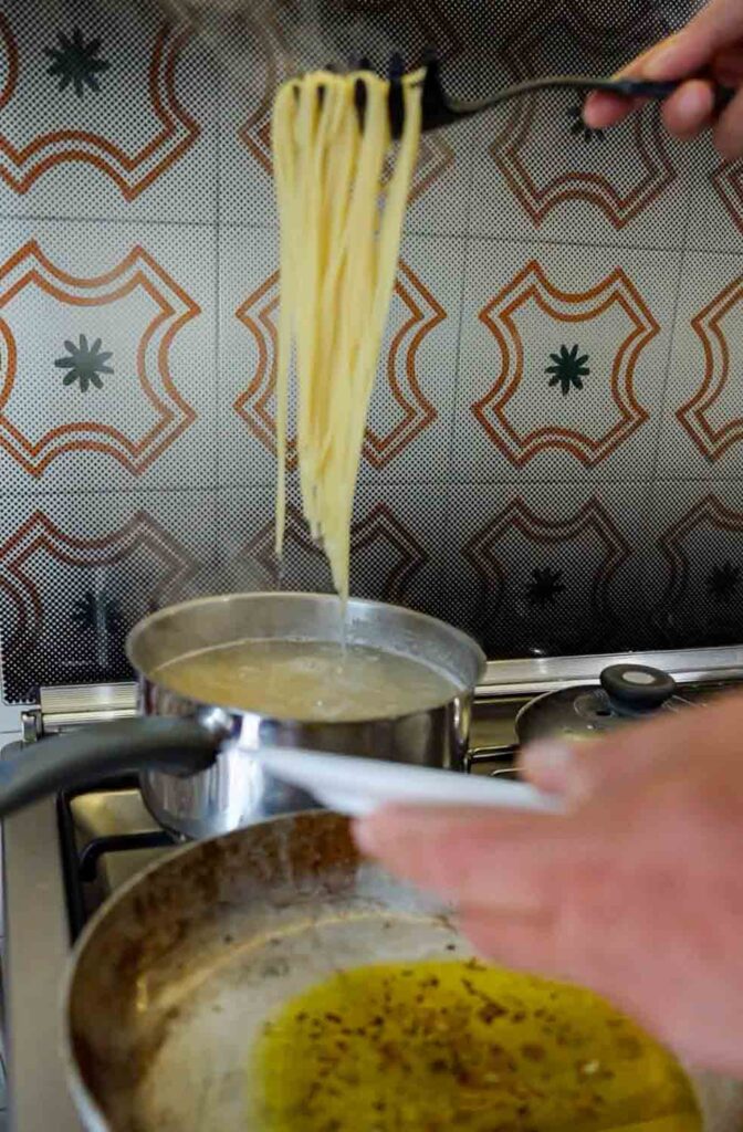 adding pasta to pan of infused oil